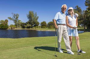Happy senior man and woman couple together playing golf on a course near a lake